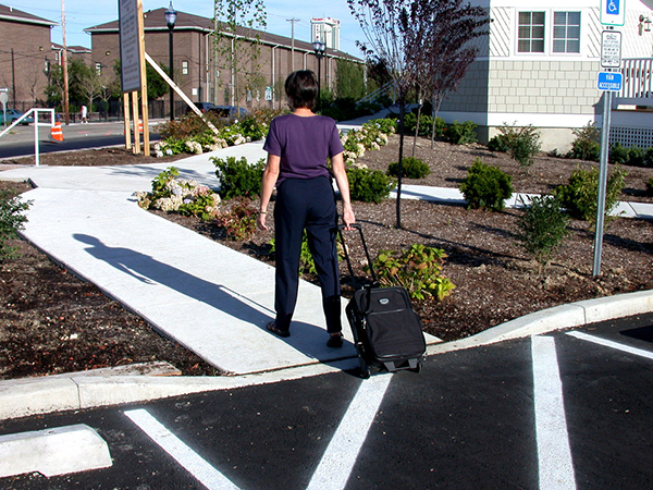 woman pulling luggage on wheels up a curb cut and gently sloped sidewalk