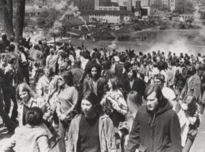 The Ohio National Guard at the bottom of a hill firing tear gas canisters into the crowds, who are walking away from the gas