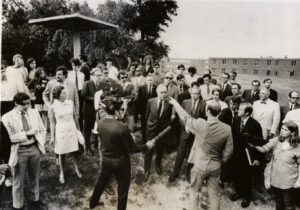 A crowd of people facing a man pointing towards something behind them