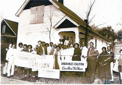 Group of people in front of a house. Signs say Union Miles Coalition