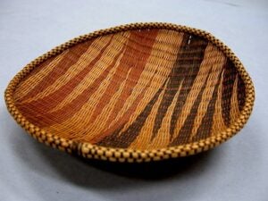 A handwoven circular food tray from Rwanda made of natural fibers in brown, tan, and red patterns.