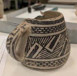 Photograph of mug (1200s), a partially chipped old mug with geometric patterns of parallel lines and rectangles.