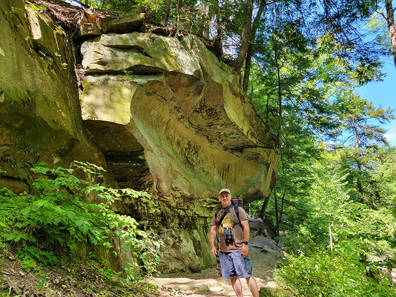 Large sandstone cliff overhanging hiker on trail at South Chagrin Reservation