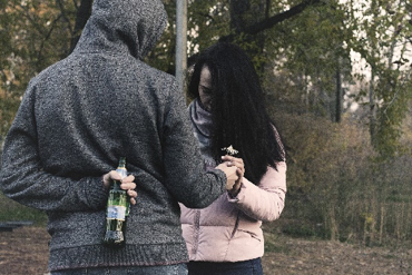 man and woman holding hands with man holding a bottle behind his back