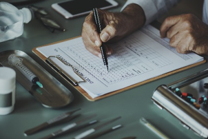 person holding pen with and writing on a clipboard