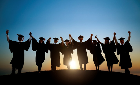 students in graduation regalia while the sun sets on the horizon
