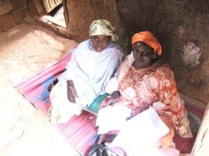 2 women seated on a rug on the floor holding interview papers.