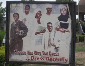 A billboard showing 6 well-dressed people who are carrying books. The text on the sign says "Choose the Way you Dress...Dress Decently